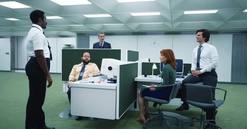 Office scene with people gathered around modern green and white cubicles.