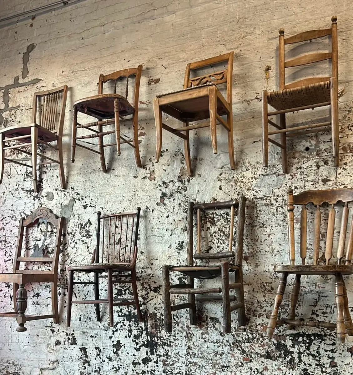 A collection of vintage wooden chairs displayed against a distressed brick wall.