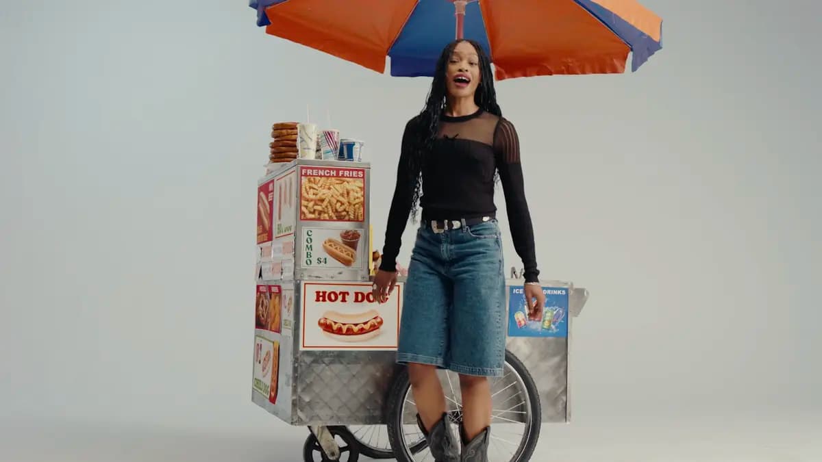 A woman standing beside a colorful New York hot dog cart used as a production prop.