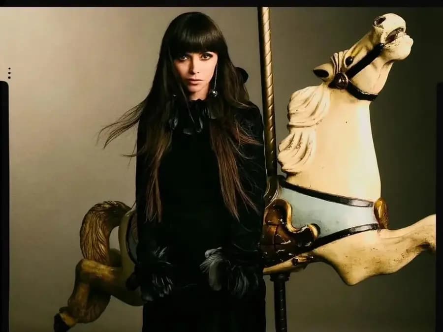 A model dressed in black standing beside a vintage carousel horse.