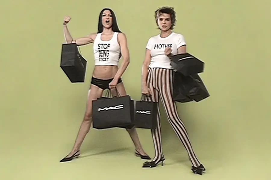 Two models holding MAC Cosmetics bags against a bright yellow backdrop.