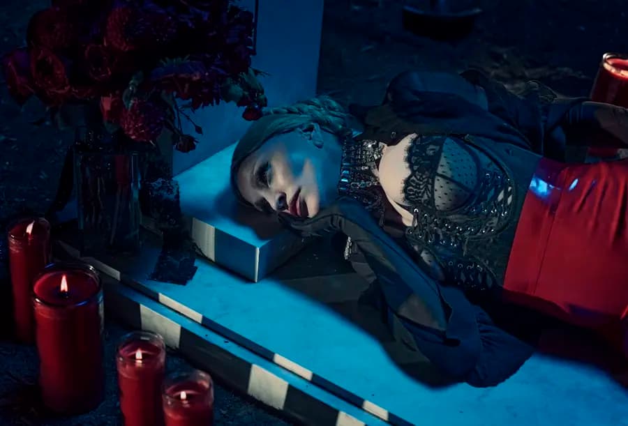 A dark fashion production set with a marble tombstone, flowers, and red candles.